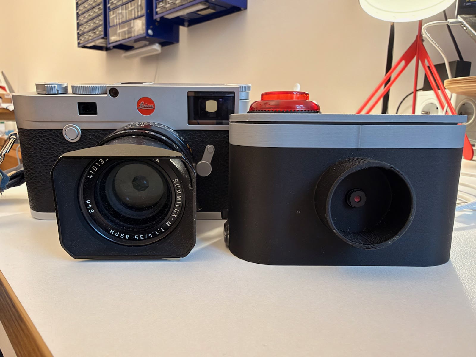 PotatoCam, black with a gray top and a big red button, standing next to a silver and black Leica with a large lens.